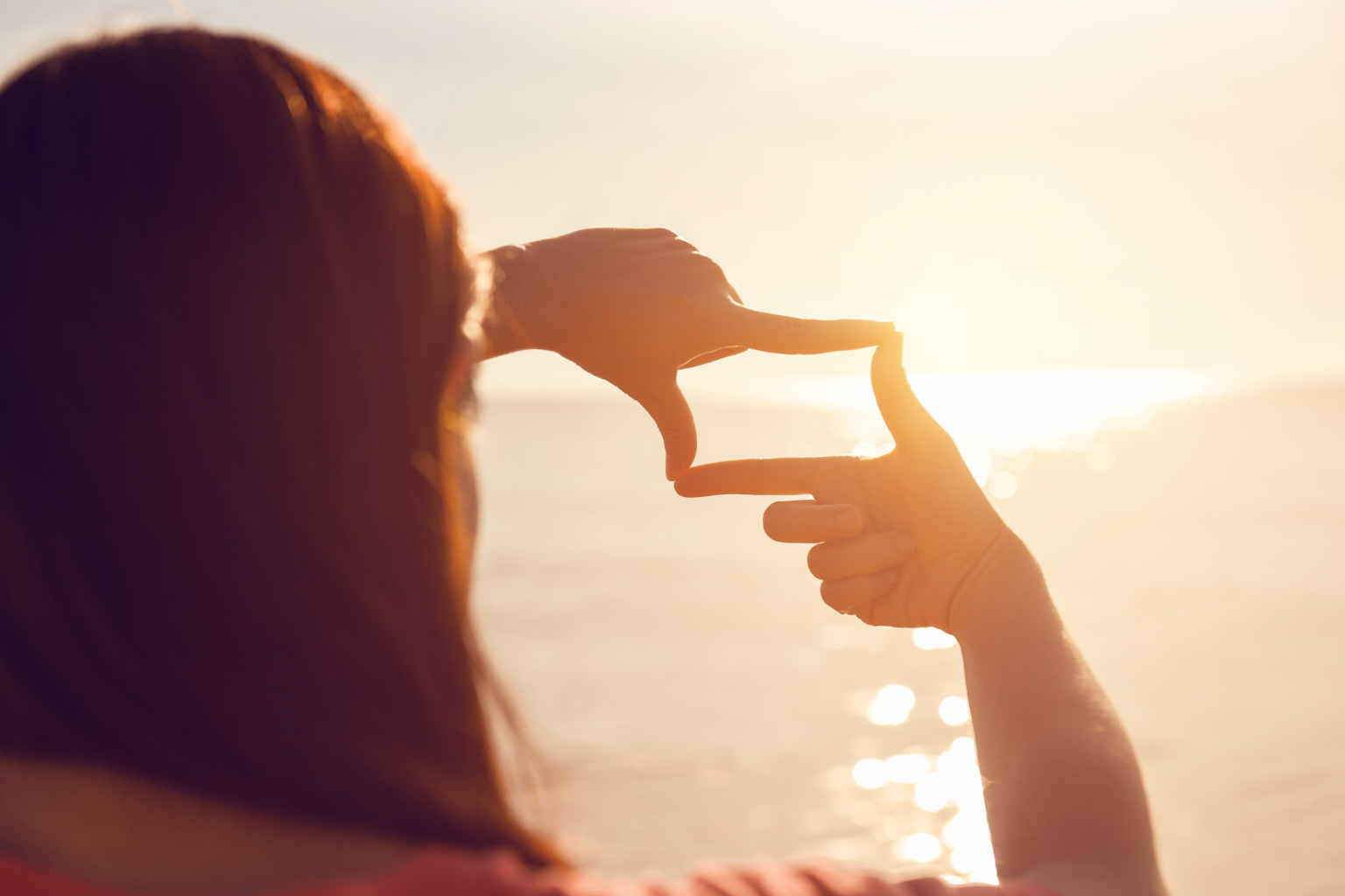 Frau blickt in die Sonne und formt mit ihren Händen einen Rahmen – Symbol für Fokus, neue Perspektiven und Zielklarheit.