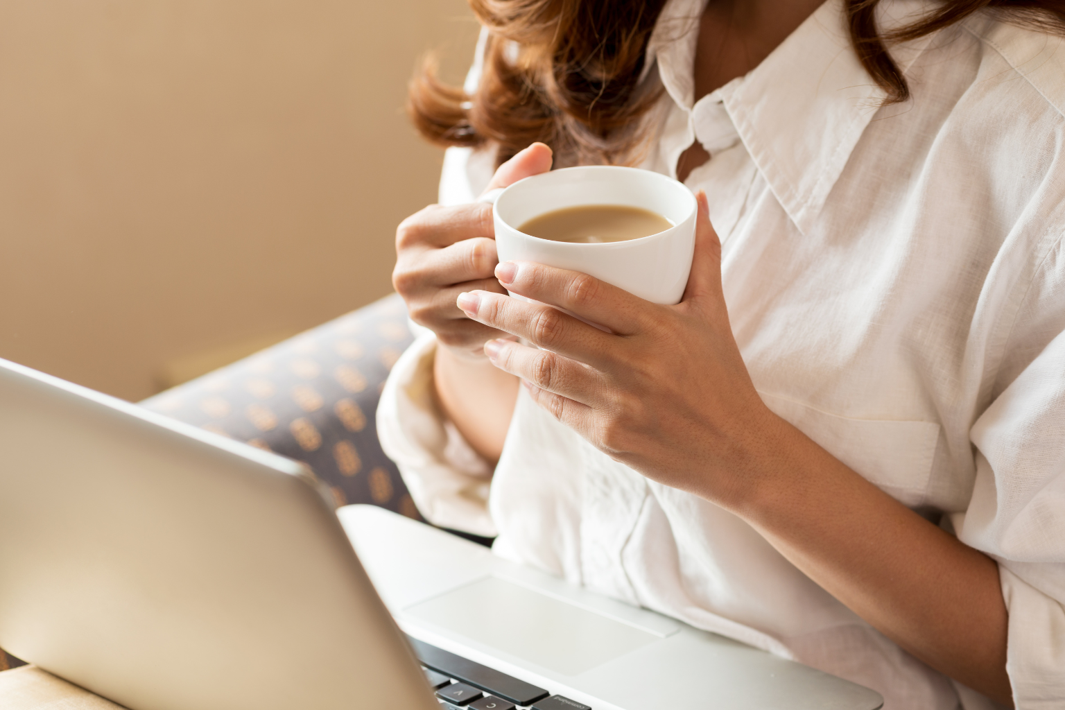 Frau mit Laptop und Tasse Kaffee beim Online-Coaching zuhause