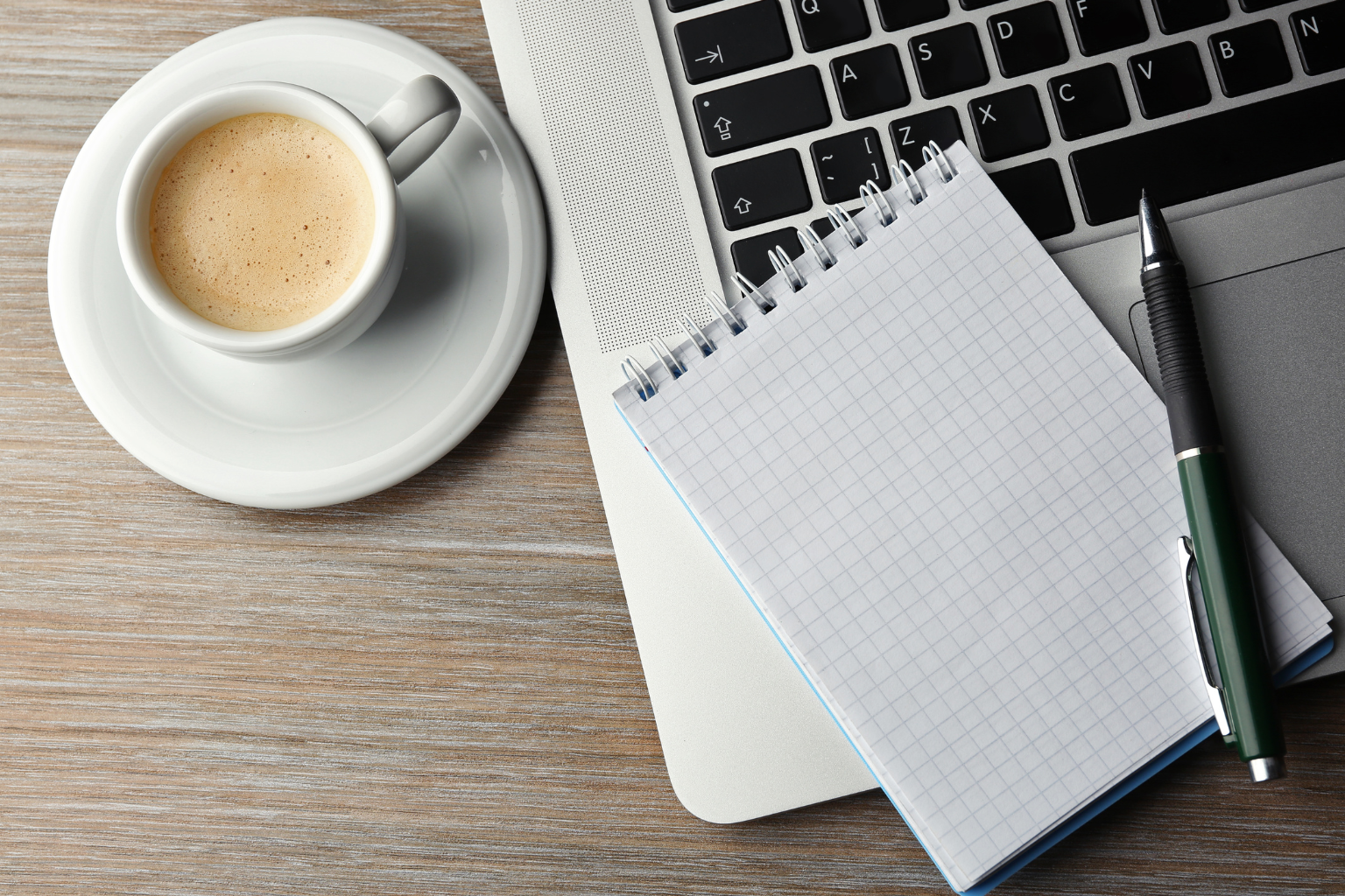 Laptop mit Notizblock, Stift und Kaffeetasse auf einem Schreibtisch