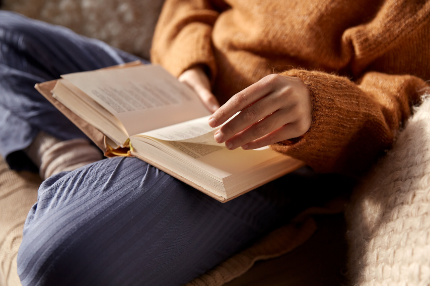 Eine Frau sitzt gemütlich auf dem Sofa und blättert in einem offenen Buch.