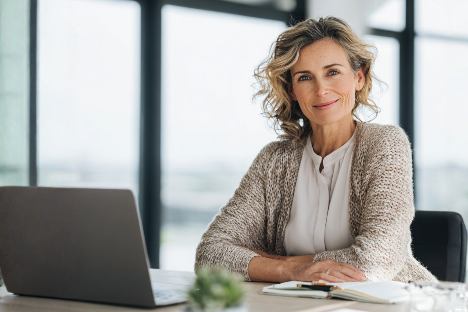 Selbstbewusste Frau Mitte 40 sitzt an einem Schreibtisch mit Laptop und Notizbuch im modernen Büro – Symbolbild für Wiedereinstieg in den Job bei der Andrea Ruisinger Akademie, Coaching online & deutschlandweit